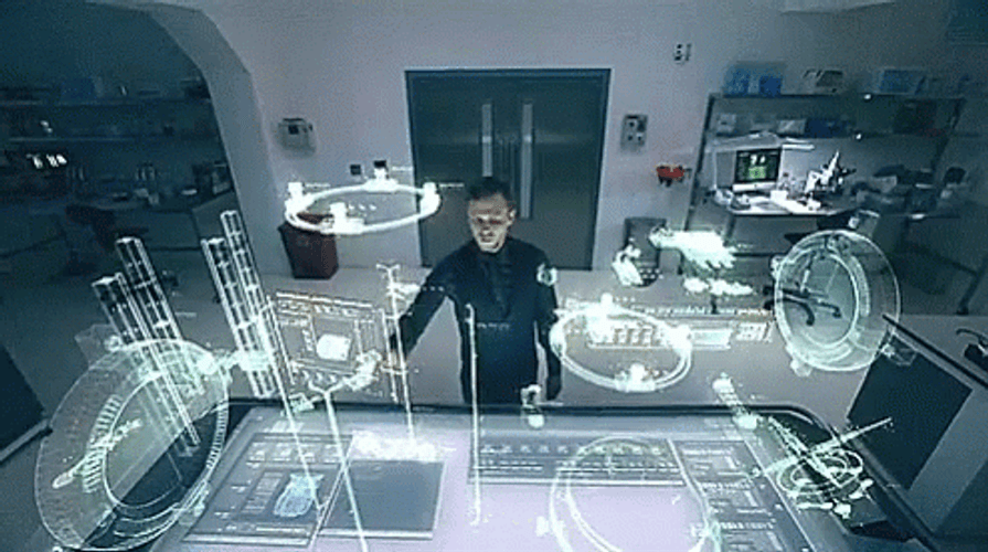 A person stands in front of a futuristic holographic interface, manipulating various glowing diagrams and technical schematics projected into the air. The scene suggests advanced technology or scientific research.