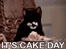 A black cat is sitting at a table with a plate of cake, happily eating it. The cat has some frosting on its face. The text "IT'S CAKE DAY" appears in the image, emphasizing the celebration of cake day.