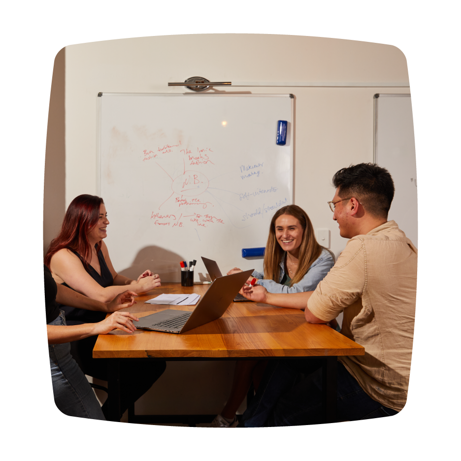 A group of four people engaged in a discussion around a table, with laptops and notes