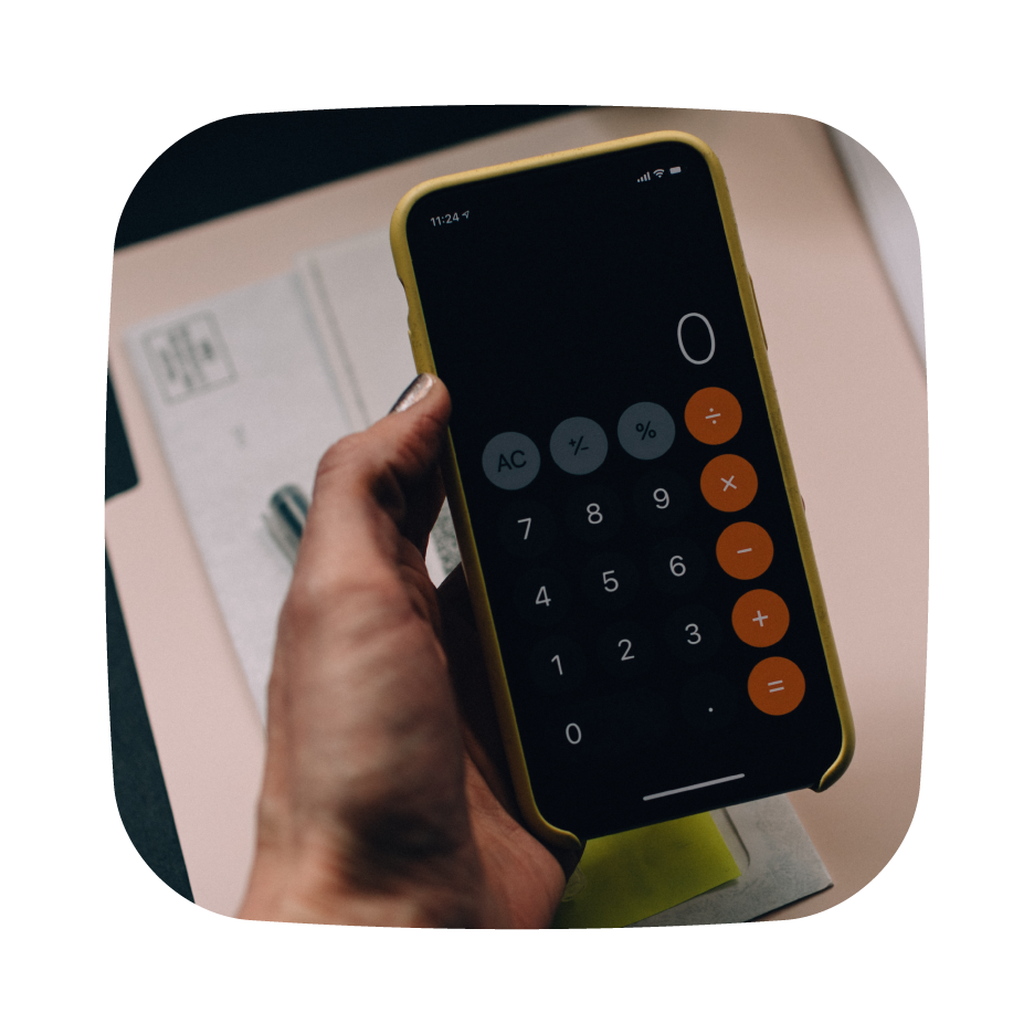 Person holding a smartphone displaying a calculator app, with documents and a pen in the background