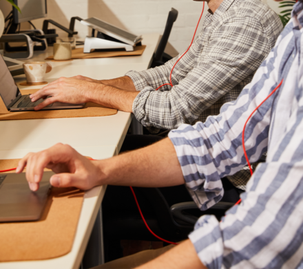 Two people working side-by-side on laptops, showcasing a collaborative work environment.