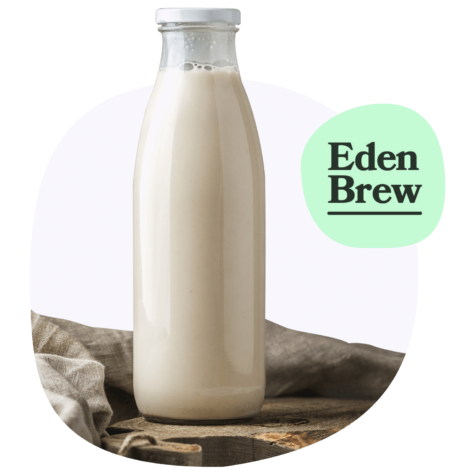 An image of a glass bottle filled with milk, placed on a wooden surface. The label reads "Eden Brew,"