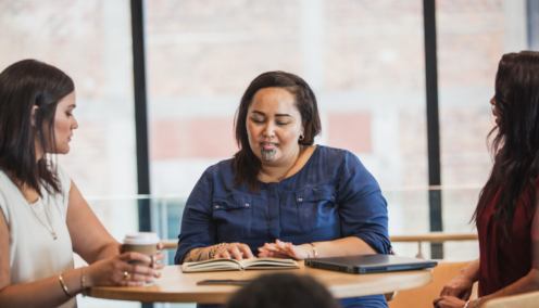 A Maori woman sits at a table in an office, discussing with two colleagues