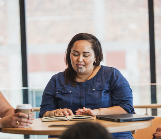 A Maori woman sits at a table in an office, discussing with two colleagues