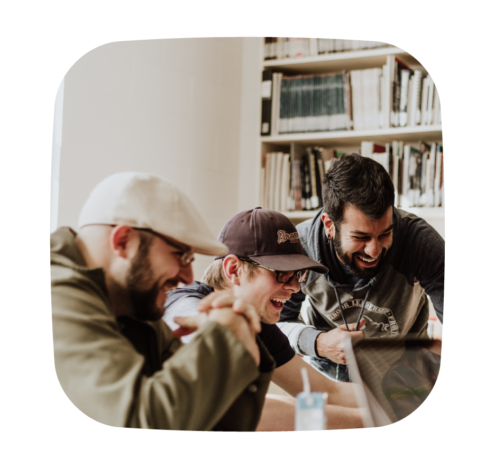 A photo of three men sitting together, smiling and laughing while looking at a laptop