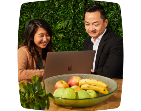 A photo of two people sitting together, smiling and looking at a laptop
