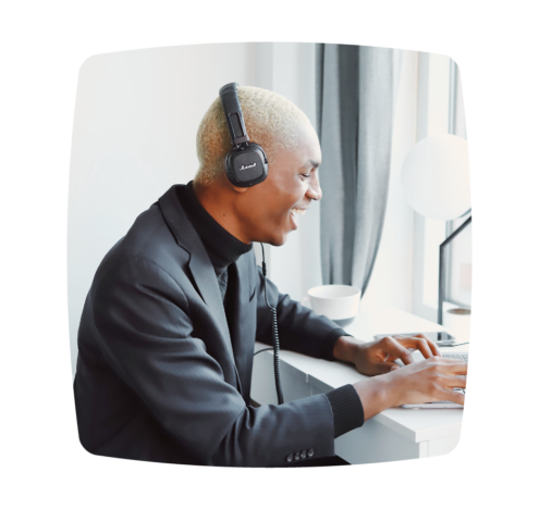 A photo of a person wearing headphones, smiling while working on a laptop at a desk